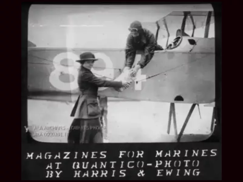 War Services Committee Librarian handing stack of magazines to courier on biplane at MCB Quantico, VA. Caption reads: Magazines for Marines at Quantico - Photo by Harris &amp; Ewing